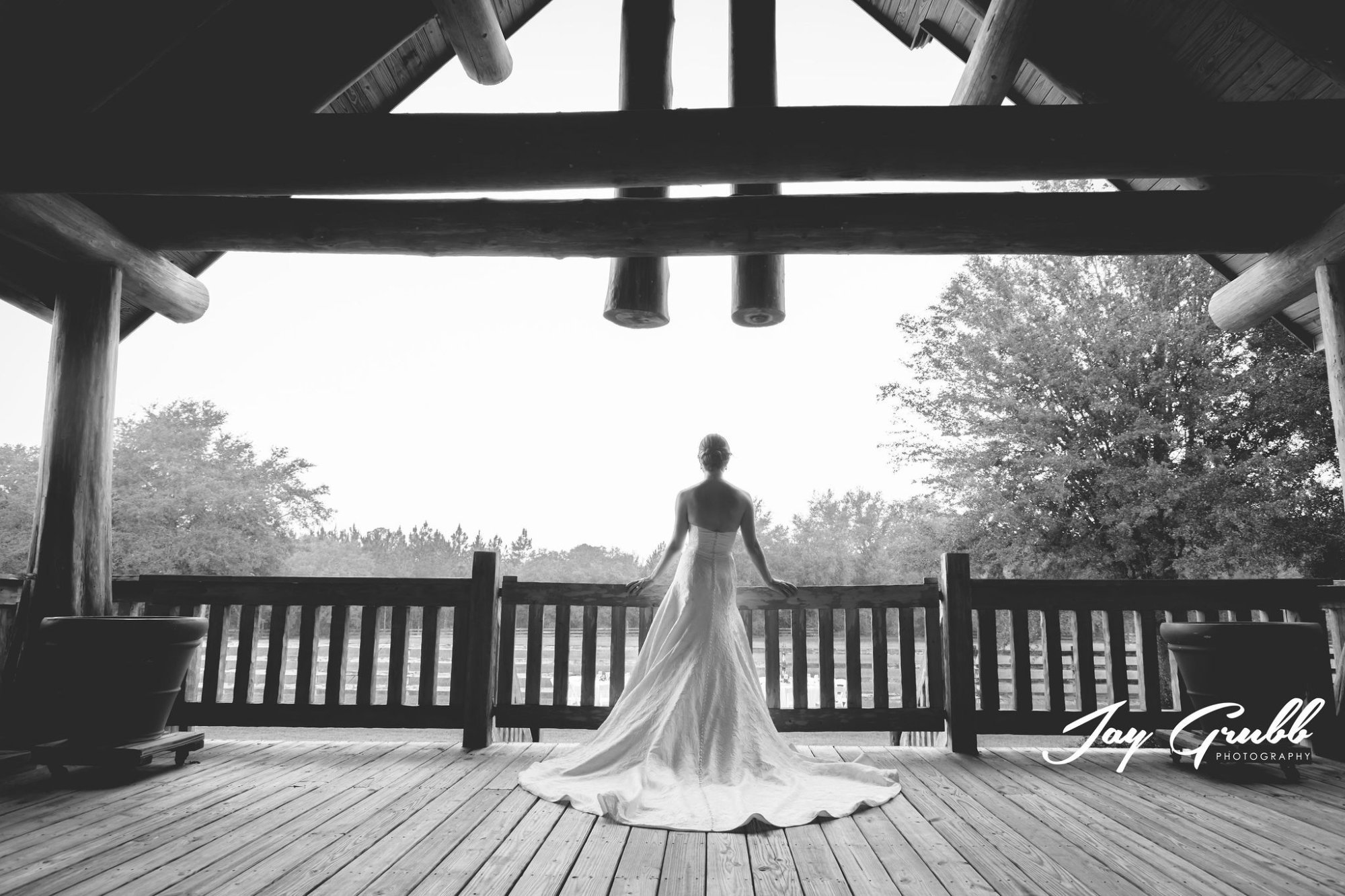 Black-and-white portrait of the bride from behind, dress spread across the porch