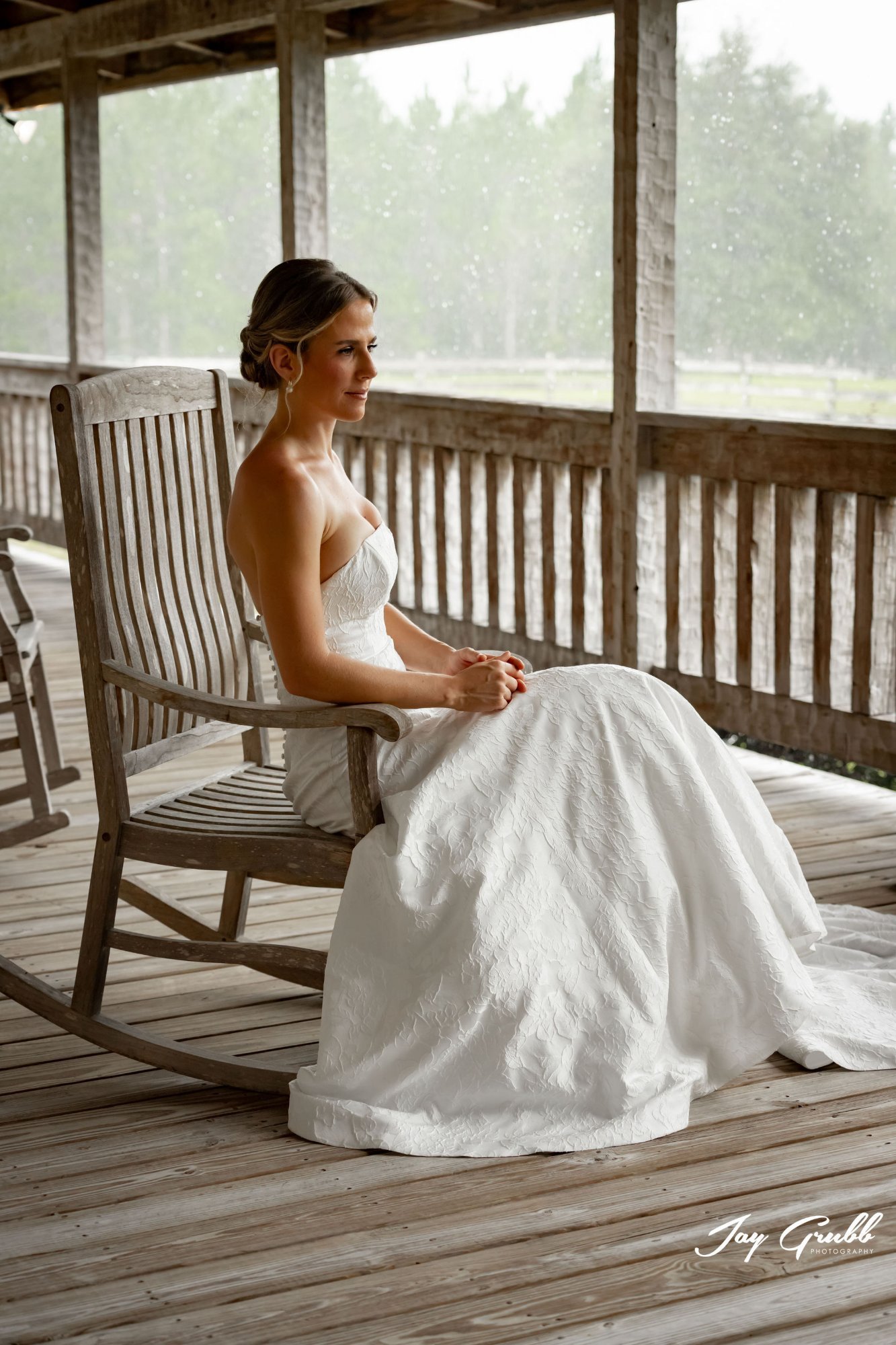 Bride in a lace gown resting in a rocking chair on the covered porch of the ranch house