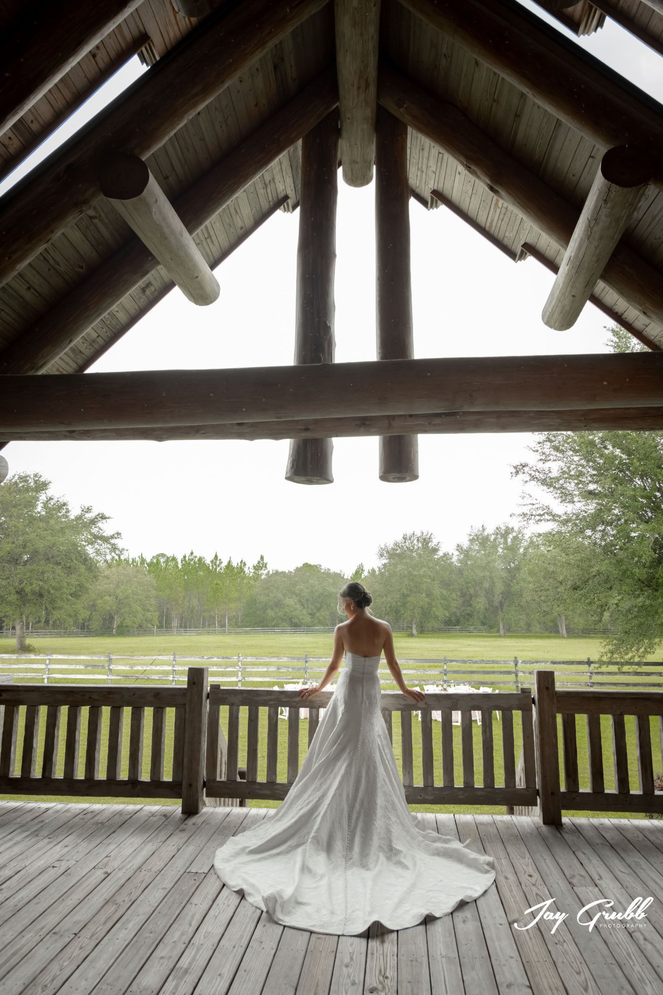 Bride on the covered porch looking out over the pastures toward the treeline