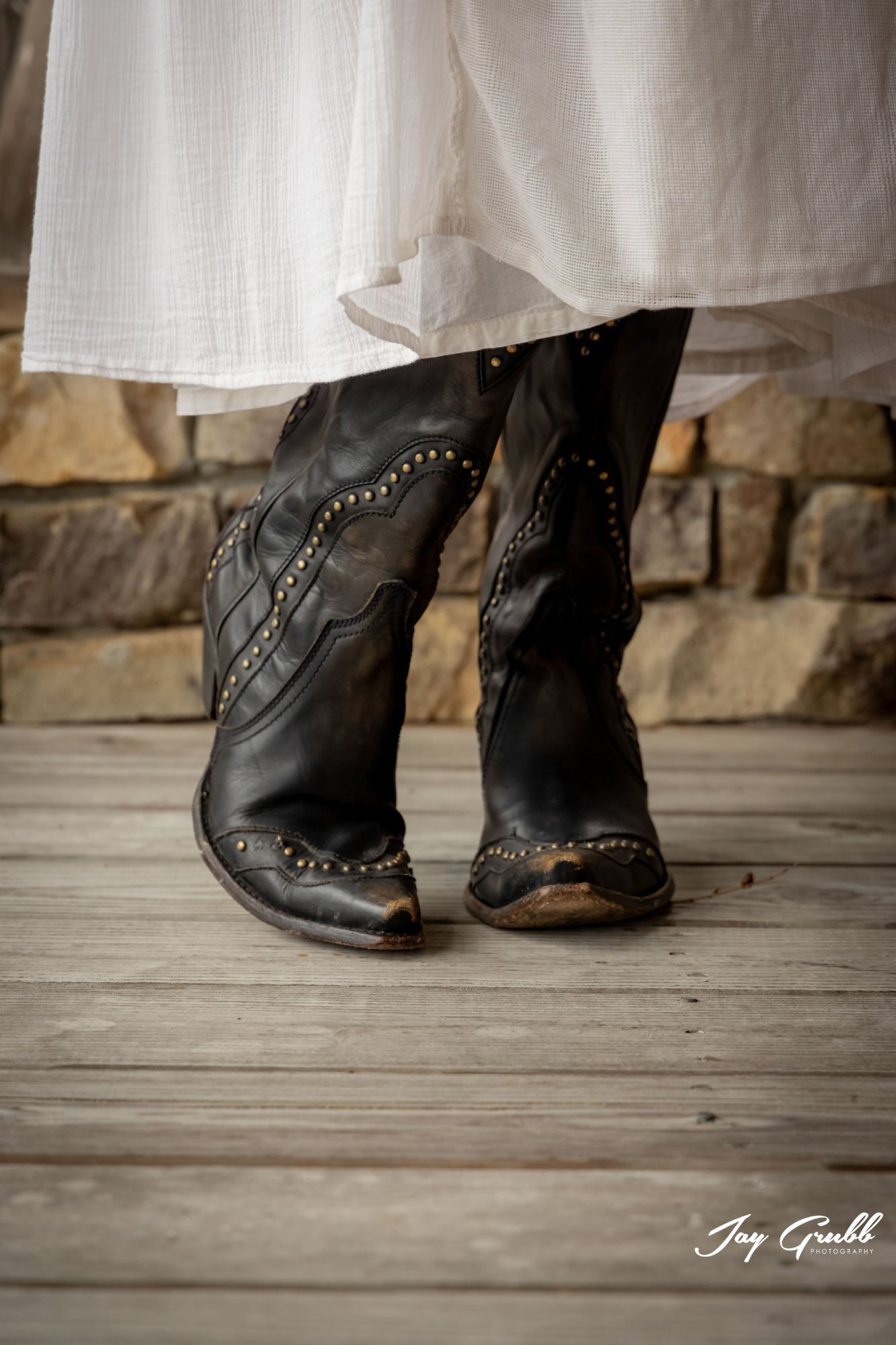 Close-up of an oval engagement ring on the bride's hand, held by the groom, in front of the weathered ranch house doors